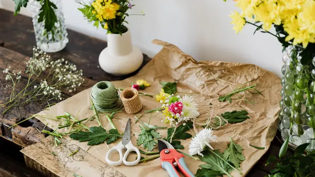Table d’atelier : papier kraft, ficelle, sécateur et fleurs coupées