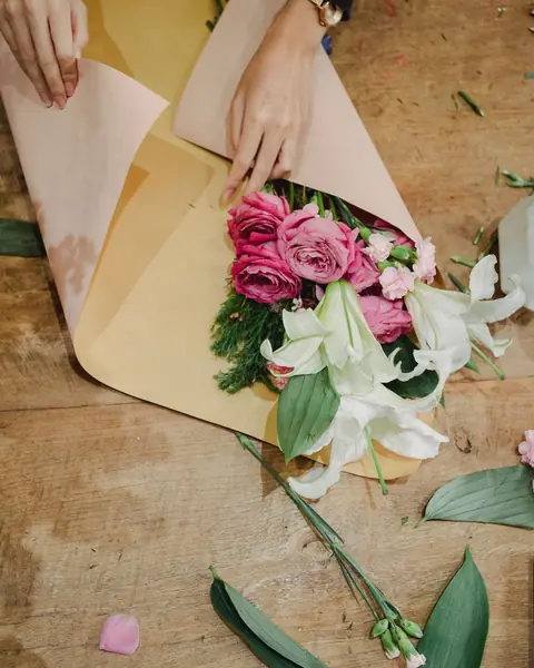 Mains qui emballent un bouquet de roses et de lys dans du papier kraft
