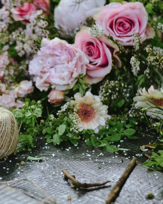 Roses et pivoines roses sur une table d’atelier, à côté d’une pelote de ficelle